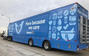 Outside Blue Walmart Mobile Pharmacy Facility With Decorative Wrap That Reads "Here because we care"